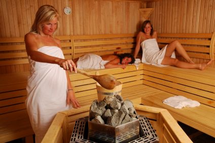 Women making steam by pouring water over sauna rocks